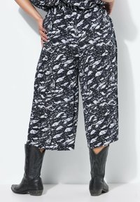 Pantaloni a gamba larga in bianco e nero con un elastico in vita, caratterizzati da un tessuto texturizzato e tasche laterali esterne. Inclusi un paio di stivali neri.