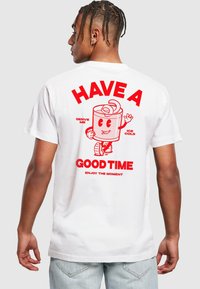 T-shirt en coton blanc avec un personnage de boisson en cartoon rouge vif dans le dos, accompagné du texte : "PASSE UN BON MOMENT" et "SERS-MOI BIEN FRAIS".