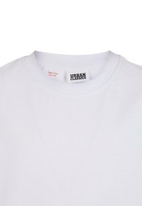 Balta kokvilnas T-krekls ar apaļu kakla izgriezumu un etiķeti ar kopšanas instrukcijām. Gluda tekstūra ar minimāliem dizaina elementiem.