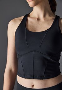Czarny crop top o dopasowanym kroju, wykonany z gładkiego materiału, z okrągłym dekoltem i subtelnymi detalami szwów z przodu.