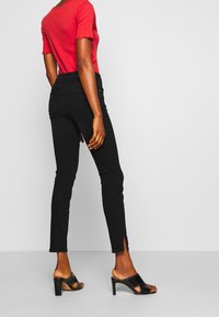 Vaqueros negros ajustados de cintura alta con aberturas laterales, combinados con una blusa roja de manga corta con canalé y mule negro con tacón. Textura suave.