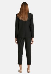 Completo giacca e pantaloni neri con giacca aderente, spalle strutturate e pantaloni alla caviglia su misura. Tessuto liscio, dettagli minimi e design elegante.