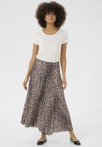 Maxirock im beigefarbenen und schwarzen Leopardenmuster, aus plissierter Stoffqualität, kombiniert mit einem weißen T-Shirt mit kurzen Ärmeln und schwarzen Ballerinas.