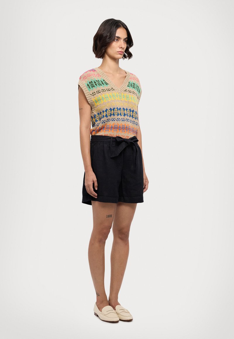 Top din tricot cu dungi multicolore în roz, verde, albastru și portocaliu. Asortat cu pantaloni scurți negri, talie legată și pantofi slip-on.