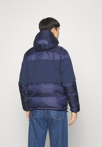 Granatowa kurtka puchowa z kapturem, z kontrastowymi panelami i pikowanym wzorem. Gładka tekstura, zaprojektowana dla ciepła i komfortu.