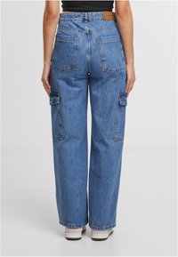 Pantalones cargo de mezclilla de pierna ancha en azul claro con bolsillos laterales dobles, bolsillos traseros y una cintura alta. Presenta una etiqueta de marca marrón en la parte trasera.
