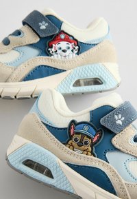 Niebieskie i beżowe dziecięce sneakersy wykonane z zamszowych i siateczkowych materiałów. Posiadają kolorowe naszywki z postaciami i rzepy do zapięcia.