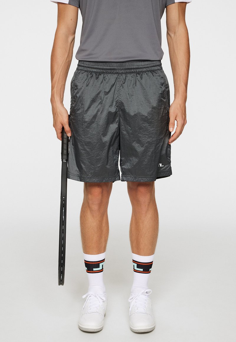 Svarta lätta träningsshorts med resårmidja, i kombination med vita strumpor som har en flerfärgad geometrisk mönstring och vita sneakers.