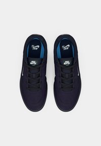 Sötét tengerészkék anyagból készült Nike SB sportcipők fekete fűzőkkel és kék belső résszel. Oldalán fehér logóval és fekete talppal rendelkezik.