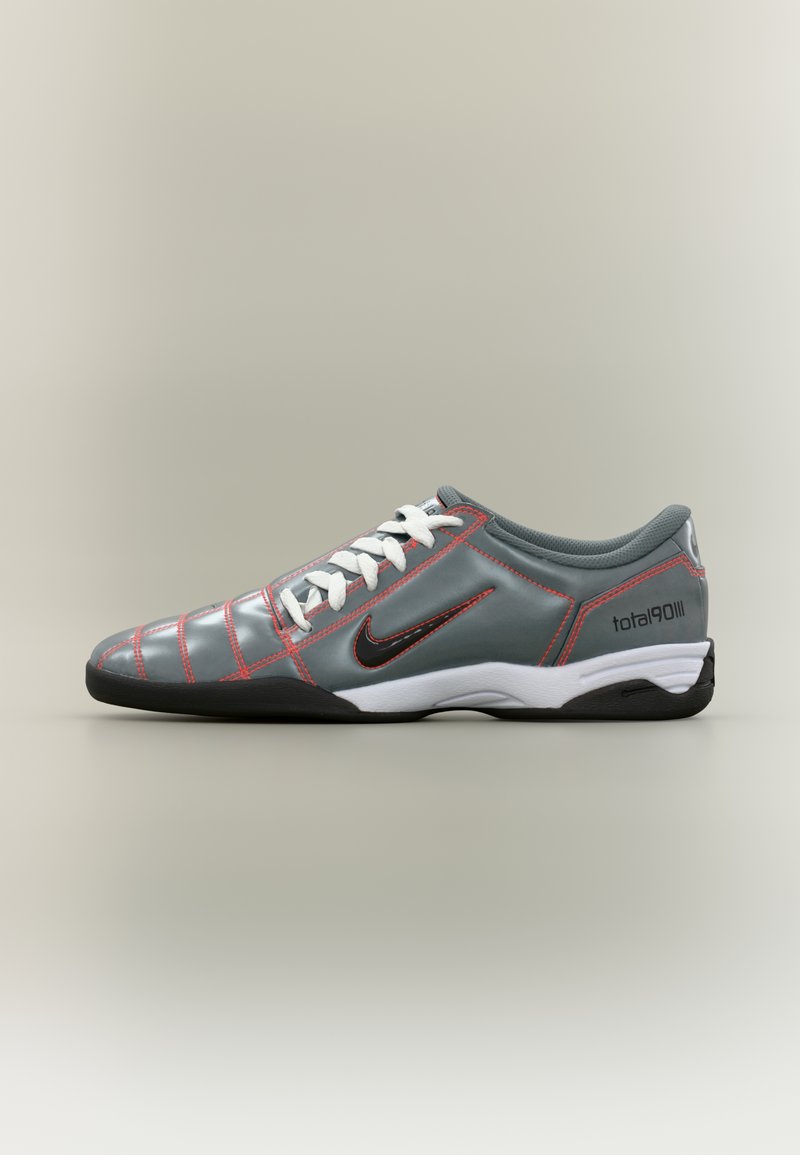 Γκρι εσωτερικό παπούτσι ποδοσφαίρου Nike Total 90 III με λευκά κορδόνια, μαύρη σόλα, κόκκινα ράμματα και μαύρο λογότυπο Swoosh στο πλάι.