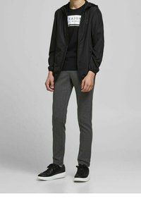 Schwarze Kapuzenjacke, schwarzes Grafik-T-Shirt, graue Slim-Fit-Sweatpants und schwarze Sneaker mit weißen Sohlen. Einfaches und funktionales Design.