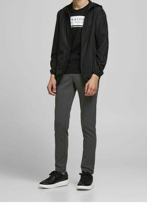 Černá kapucínová bunda, černé grafické tričko, šedé slim-fit tepláky a černé tenisky s bílými podrážkami. Jednoduchý a funkční design.