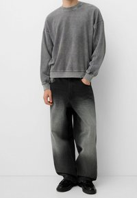 Šedá fleecová mikina s kleslými rameny v kombinaci se širokými gradient šedými džíny. Černé boty dokončují tento outfit.