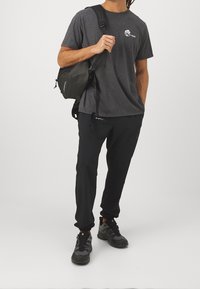 Gray cotton t-shirt with logo, black athletic pants, and black backpack; textured sneakers with gray and black accents.