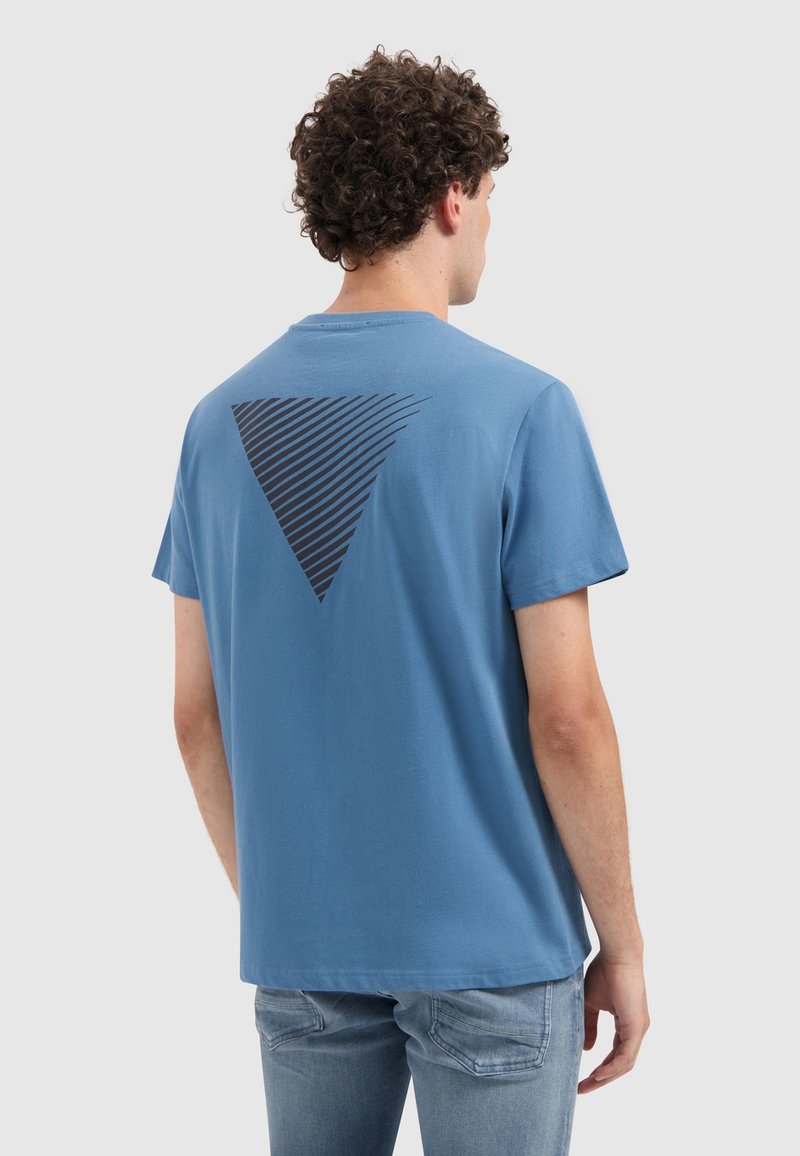 Blauwe katoenen T-shirt met korte mouwen, featuring een grote zwarte driehoekige grafiek op de achterkant, tegen een effen lichte achtergrond.