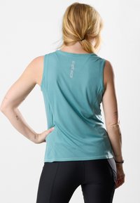 Top senza maniche di colore azzurro chiaro, con tessuto testurizzato, scollatura tonda e un piccolo'etichetta con logo sul retro. Indossato con leggings neri.