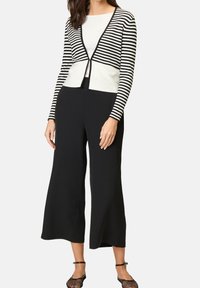 Czarne szerokie spodnie połączone z kardiganem w czarno-białe paski, z dekoltem w serek i zapięciem na guziki z przodu.