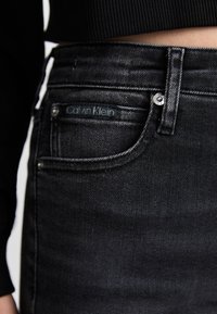 Crne traperice od denima s glatkom teksturom, s Calvin Klein oznakom na prednjoj džepu i klasičnim dizajnom s pet džepova.