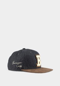 Graue Wollmütze mit einem braunen Wildleder-Schirm. Mit gesticktem 'B'-Emblem und dem Text "Bavarian Caps" in weißer Stickerei.