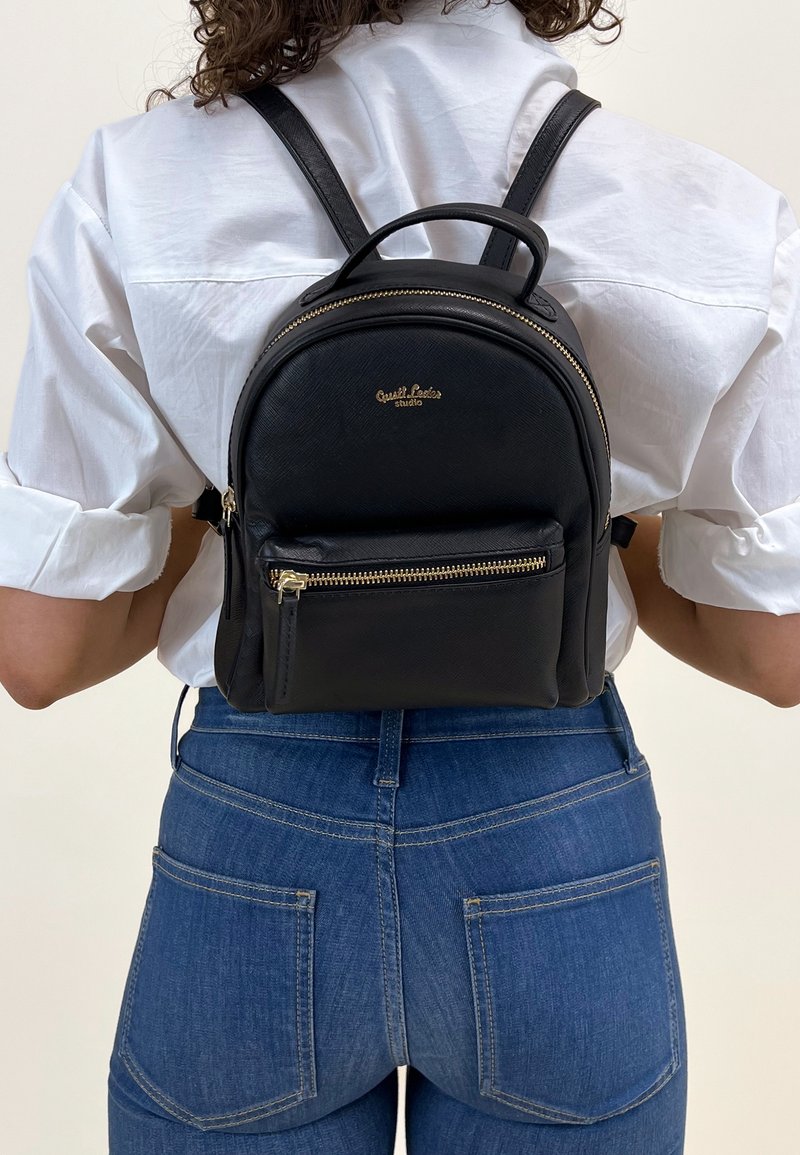 Zaino in pelle nera con forma arrotondata, dotato di una tasca frontale con zip, accessori in oro e spallacci regolabili.