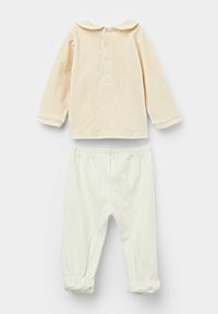 Jasnobeżowa bluzka z długim rękawem, okrągłym kołnierzykiem i zapięciem na guziki, zestawiona z białymi spodniami na gumce w pasie, z marszczonymi mankietami.