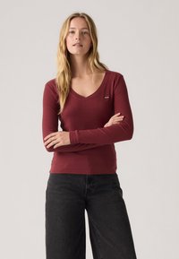 Bordeaux langermet t-skjorte med V-hals, med en liten Levi's-logo på venstre bryst. Kombinert med sorte vide jeans.