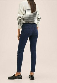 Úzké tmavě modré džíny vyrobené z denimu, doplněné krémovým svetrem s námořnickými pruhy a černými mokasíny, ukazující elegantní siluetu.