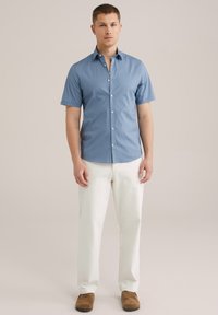 Camisa de botones de manga corta de color azul claro con cuello estándar, combinada con pantalones blancos y zapatos marrones, que muestra líneas limpias y un ajuste casual.
