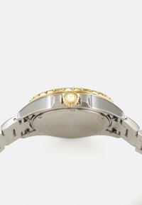 Sølv rustfrit stål ur med en guldfarvet bezel og krone. Urets kasse er rund, med en glat bagside og et metalled-links armbånd.