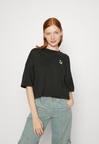 Black cropped t-shirt made of cotton with a round neckline and short sleeves. Features a small white Puma logo on the chest.