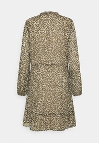 Genomskinlig klänning med långa ärmar som har ett brunt och beige abstrakt mönster. Designen inkluderar en volangkant och en insydd midja.