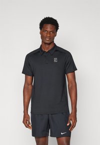 Black polo shirt with short sleeves and a collar, featuring a small white logo on the chest. Made of a smooth, lightweight material.