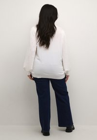 Vit tröja med texturerade, puffiga ärmar och ribbad nederkant, i kombination med mörkblå vida jeans och svarta ankelstövlar. Slät tyg.