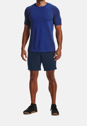 Niebieska sportowa koszulka z krótkimi rękawami i delikatnym paskowanym wzorem, w połączeniu z granatowymi szortami i czarnymi butami sportowymi.