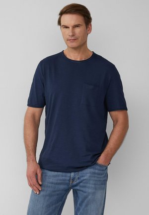 Marineblauwe T-shirt met korte mouwen, gemaakt van zachte stof, met een ronde halslijn en een kleine, eenvoudige borstzak. Draagt met lichtblauwe jeans.