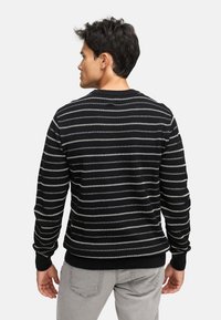 Stribet sort og hvid sweater med rund hals, ribbede manchetter og kant. Strikket tekstur med vandrette linjer, der varierer i bredde.