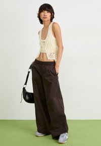 Crochet crop top in cream with tie detail, paired with loose-fitting dark brown pants. Accessorized with a small black bag and gray sneakers.