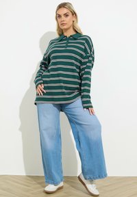 Zielono-biały w paski, długi rękaw, polo w połączeniu z jasnoniebieskimi szerokimi spodniami dżinsowymi i białymi trampkami, na tle czystego tła.