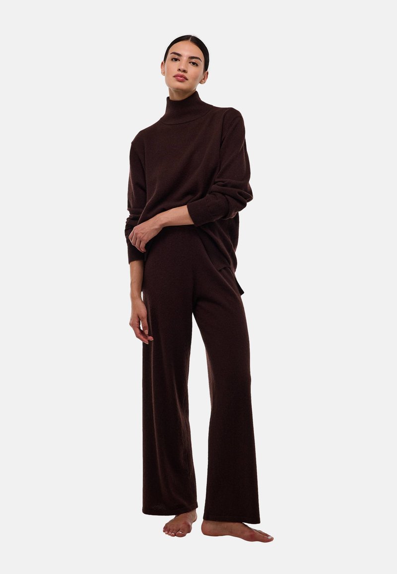 Un pull col roulé en maille marron associé à un pantalon large, tous deux présentant une texture douce. La tenue a un design décontracté et ample.