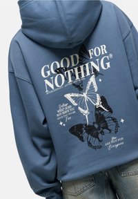 Cotton hoodie in muted blue with a large butterfly graphic. Features "GOOD FOR NOTHING" text in white and black designs. Hooded with a relaxed fit.