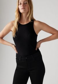 Top negro de canalé con escote redondo, combinado con jeans negros ajustados. La tela parece suave, con costuras y acentos mínimos.