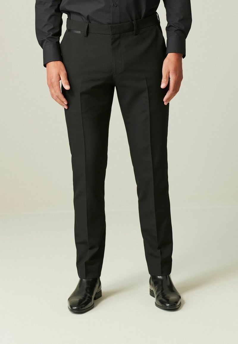 Pantalones negros ajustados con un corte slim, con parte delantera plana y bolsillos laterales, combinados con botas de vestir negras brillantes.