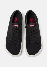 Sneakers neri in tela con superficie texturizzata, dotati di lacci piatti, una suola in gomma bianca e il marchio rosso "Camper" sulla linguetta.