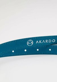 Tyrkysový kožený řemínek na hodinky s prošíváním a bílými otvory, na povrchu má stříbrné logo "AKARDO". Hladký povrch.