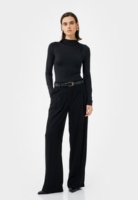 Mustapaita, jossa on pitkät hihat ja korkea kaulus, yhdistettynä leveälahkeisiin mustiin housuihin. Tyylitelty mustalla vyöllä, jossa on kultainen solki.