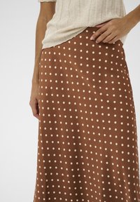 Brun nederdel med polkaprikker og et let, flydende design, med cremefarvede prikker og en glat tekstur. Ingen synlige beslag eller særlige detaljer.