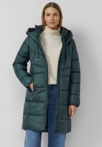 Zielona, pikowana parka z kapturem, zamkiem z przodu, dwoma bocznymi kieszeniami i kontrastowym, jaśniejszym przeszyciem. Miękki, błyszczący materiał i średnia długość.