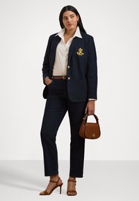 Námořnický blazer se zlatým emblémem, bílá košile na knoflíky, tmavé džíny a hnědá kabelka. Béžové sandály na vysokém podpatku.