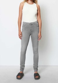 Jeans ajustados grises de mezclilla, con una cintura alta, cinco bolsillos y un diseño limpio. La modelo lleva una camiseta de tirantes de rayas blanca y sandalias oscuras.