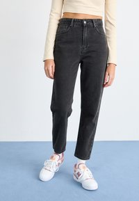 Čierne džíny so zvýšeným pásom a rovnými nohavicami, s piatimi vreckami a jemne vyblednutou textúrou, skombinované s farebnými teniskami.